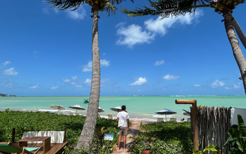Homem observa mar esverdeado da Praia de Lages, na Rota Ecológica dos Milagres, em dia de céu azul