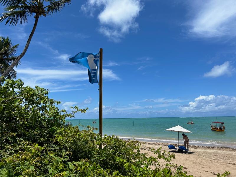 Bandeira Azul na Praia do Patacho com pessoa na areia embaixo de guarda-sol