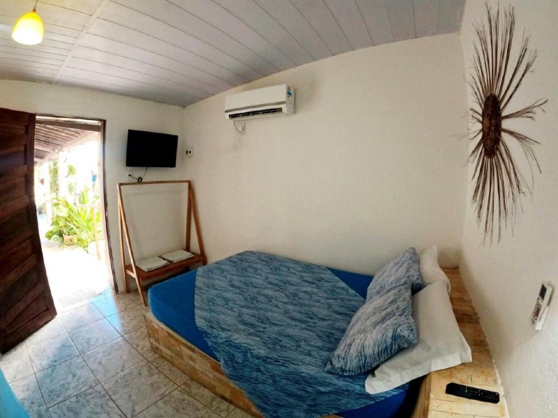 Quarto da Pousada da Vivi, dica de onde ficar em Maracaípe, com cama de casal com roupa azul, TV e ar-condicionado