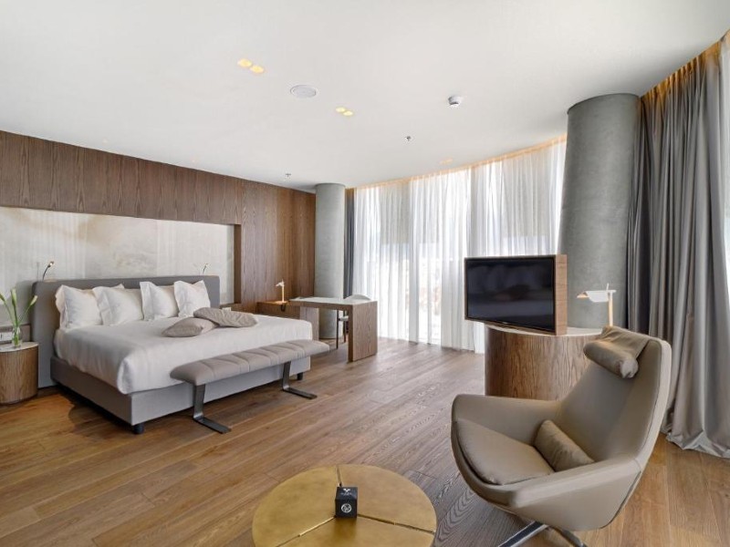 Quarto espaçoso do Maritim Hotel com cama de casal, piso de madeira, TV e poltrona