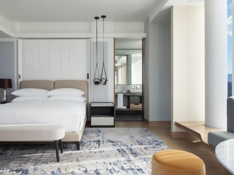 Quarto do Tirana Marriott Hotel com cama de casal, tapete no chão e paredes claras