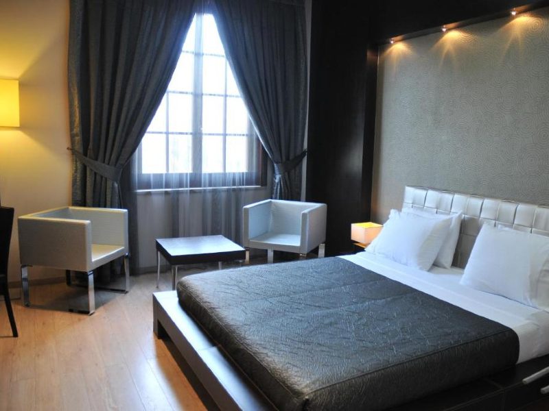 Quarto do MonarC, dica de onde ficar em Tirana, com cama de casal, duas cadeiras e uma mesa de centro perto da janela