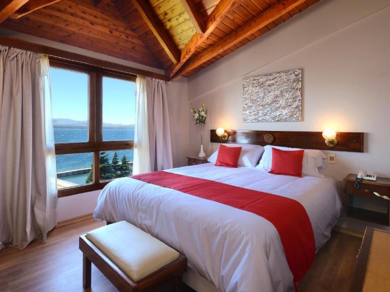 Quarto do Hotel Concorde com cama de casal, piso de madeira e vista para o lago Nahuel Huapi