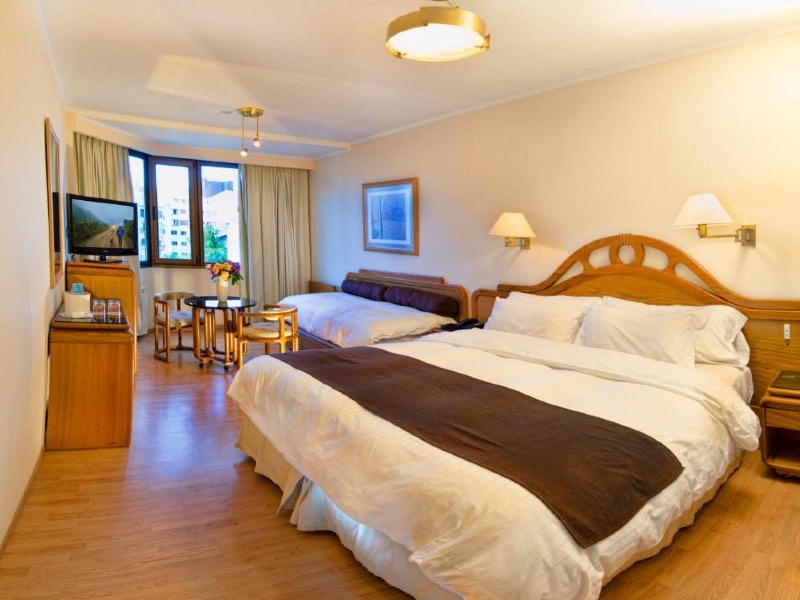 Quarto do Hotel Cristal, dica de onde ficar em Bariloche, com cama de casal, sofá-cama, TV e mesa de madeira