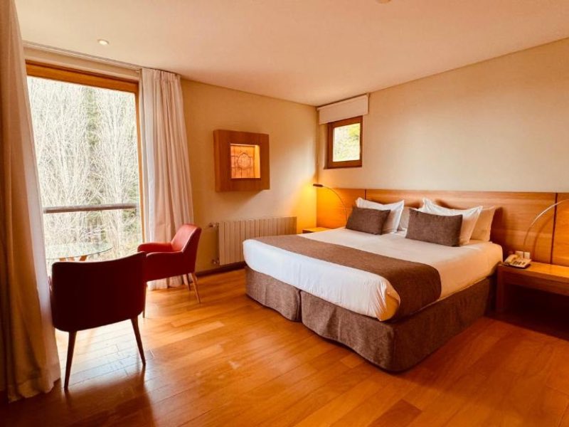 Quarto do Design Hotel, dica de onde ficar em Bariloche, com cama de casal, piso de madeira e poltrona vermelha perto da janela