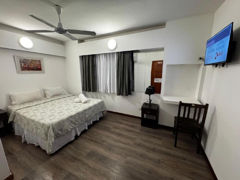 Quarto simples do NBH Premier com cama de casal, piso de madeira escuro e TV