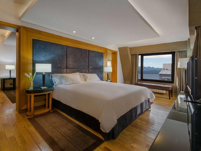 Quarto do NH Bariloche Edelweiss com cama de casal, piso de madeira e vista para o lago