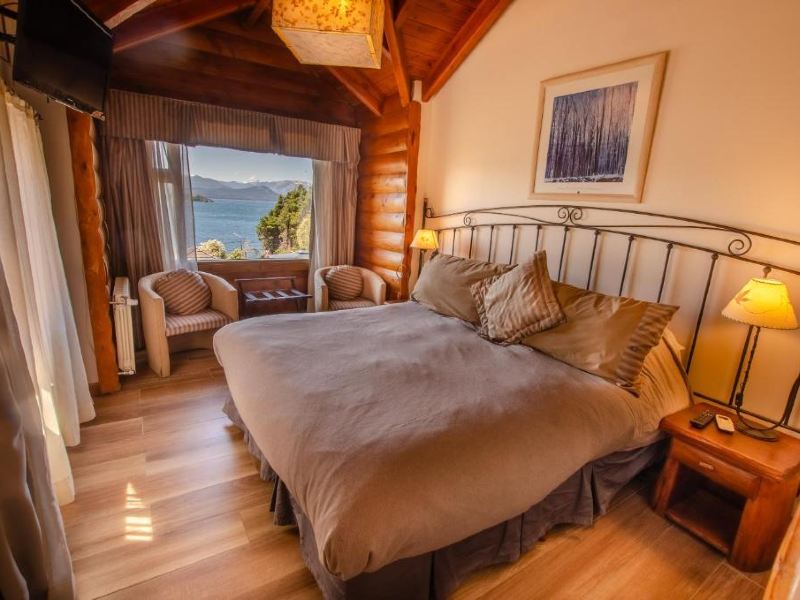 Quarto do Nido del Condor, dica de onde ficar em Bariloche, com cama de casal, poltronas, piso de madeira e vista para o lago