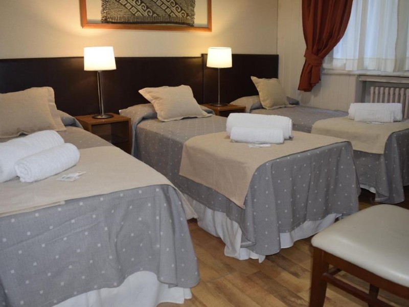 Quarto do Hotel Nórdico com três camas de solteiro, cadeira e piso de madeira