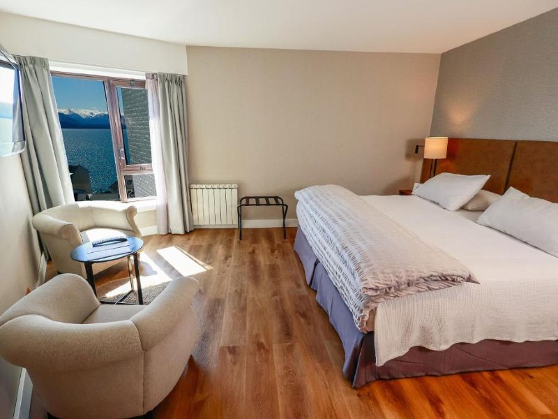 Quarto do Sheraton, dica de onde ficar em Bariloche, com cama de casal, piso de madeira, duas poltronas e vista para o lago Nahuel Huapi