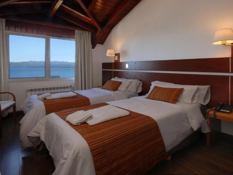 Quarto escuro do Hotel Tirol com duas camas de solteiro, decoração de madeira e vista para o lago