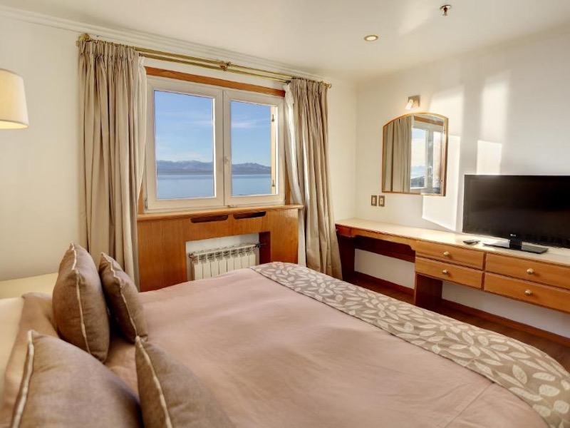 Quarto do Tres Reyes, dica de onde ficar em Bariloche, com cama de casal, móveis de madeira, TV e vista para o lago Nahuel Huapi