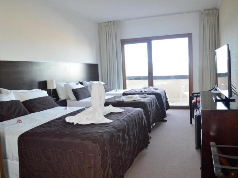 Quarto simples do View Hotel com três camas, carpete, TV e móveis de madeira