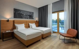 Quarto do MK Hotel, dica de onde ficar em Tirana, com duas camas de solteiro, poltrona, piso de madeira e vista para a piscina