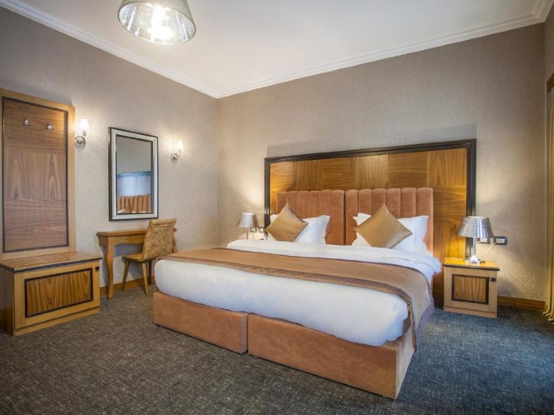 Quarto do Hotel Colosseo, dica de onde ficar em Tirana, com cama de casal, carpete e decoração em madeira
