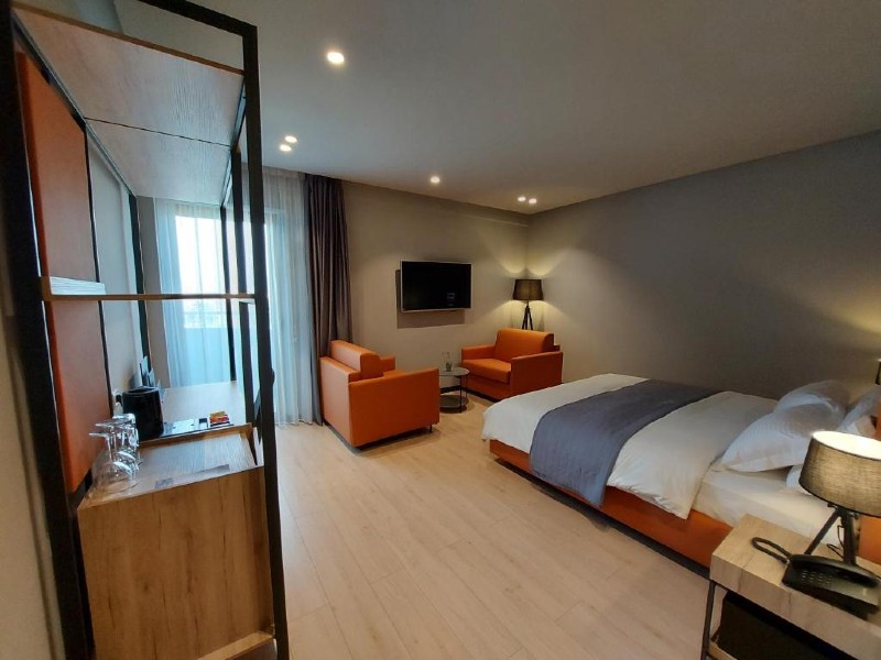 Quarto espaçoso do Mulaj, dica de hotel em Tirana, com cama de casal, duas poltronas e estante