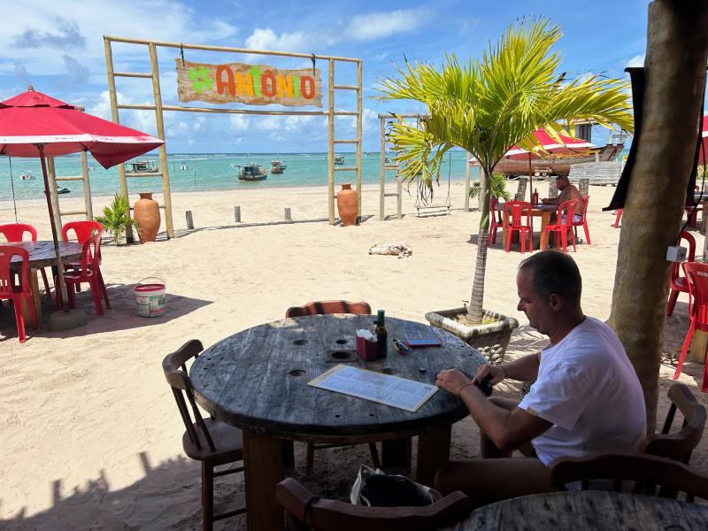 Homem sentado em mesa do Antônio Restaurante de frente para o mar em dia de sol e céu azul