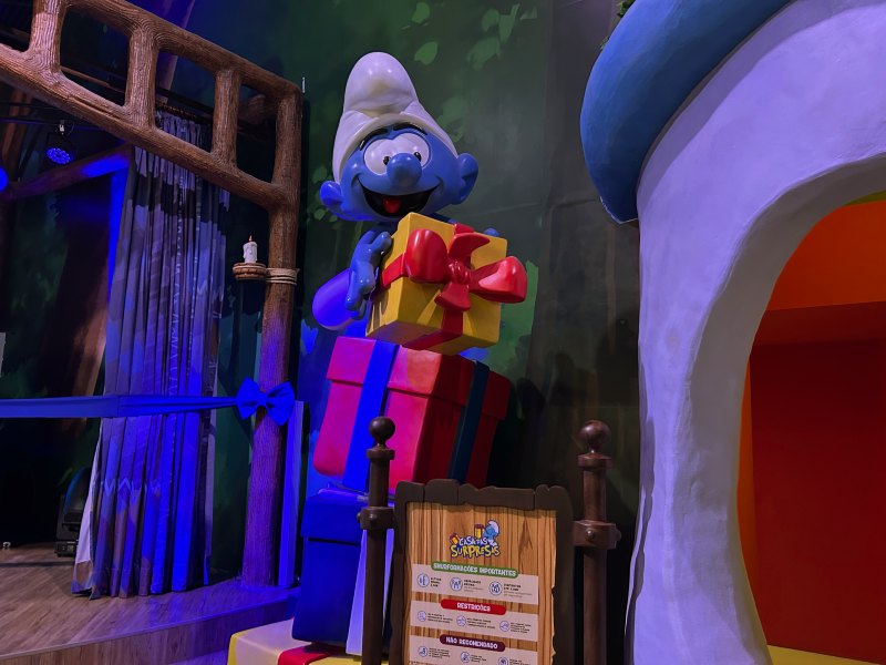 Smurf segura presente em decoração ao lado de palco em área temática dos personagens em SP